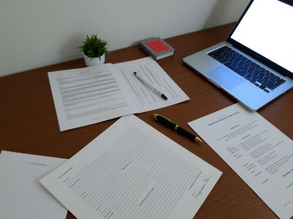 Birou ordonat, documente, laptop și pix pentru înregistrarea numelui.
